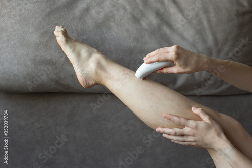 Female hands epilate one leg with an electric epilator on a brown background photo