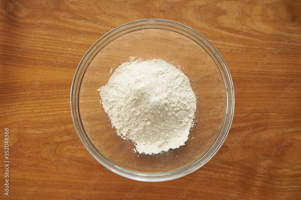 Pile of flour in a transparent glass salad bowl on wooden table top view Pile of flour in a transparent glass salad bowl on wooden table top view