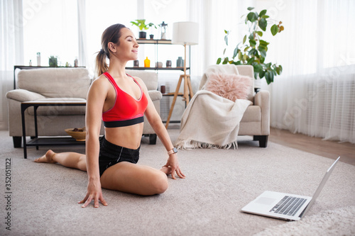 Online yoga workout at home. Attractive young woman doing stretching in living room. Sport, entertainment and education on the Internet.