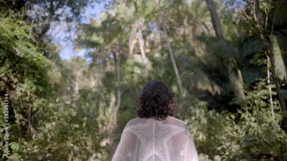 Mysterious attractive woman walks through jungle forest wearing long flowing dress inviting viewer to come along with her Mysterious attractive woman walks through jungle forest wearing long flowing dress inviting viewer to come along with her