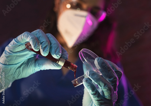 Nurse wearing hazmat suit, protective goggles and antiviral mask kn95 for covid19, dark room laboratory performs virus or antidote scan using surgical glove holding blood and coronavirus test sample