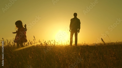 Happy healthy child with dad walk at sunset in field. Dad hugs daughter  baby plays  runs away. Silhouette of a family walking in sun. dad and baby in park. concept of happy family. Family lifestyle