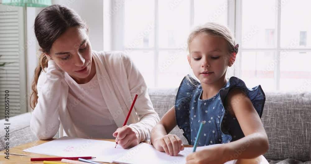 Head shot young mixed race female tutor teaching little girl drawing in paper album. Focused baby sitter nanny coloring pictures or preparing art lesson homework with school aged little girl. Head shot young mixed race female tutor teaching little girl drawing in paper album. Focused baby sitter nanny coloring pictures or preparing art lesson homework with school aged little girl.
