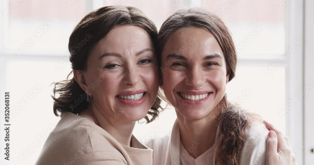 Head shot close up overjoyed smiling two bonding female generations family cuddling, looking at camera. Excited middle aged mommy enjoying funny tender moment, laughing with happy grown daughter.