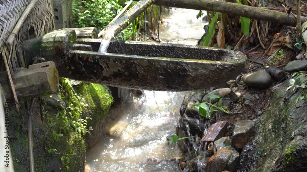 Water from a bamboo pipe flows into the river in the courtyard in the mountain village of Sapa, Vietnam, close up