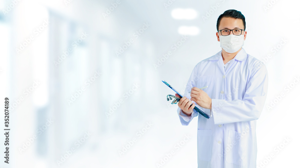 Portrait of Asian medical male Doctor wear a mask to prevent germs and standing in front of his blurred interior hallway in hospital banner background.Concept of effective work in hospitals. Portrait of Asian medical male Doctor wear a mask to prevent germs and standing in front of his blurred interior hallway in hospital banner background.Concept of effective work in hospitals.