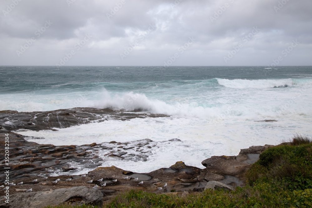 Storm in the ocean. Cloudy sky. Big waves are crashing into the rocks making white foam.