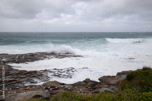 Storm in the ocean. Cloudy sky. Big waves are crashing into the rocks making white foam.