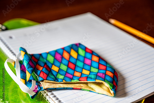 Face mask resting on top of back to school supplies of paper, pencil and a clip board photo