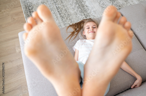 Preteen girl lying on couch with her bare feet raising up high