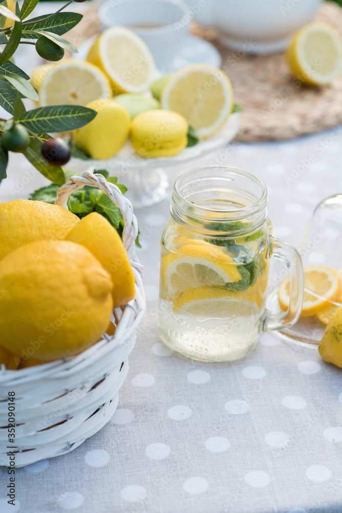 Lemonade with lemon, mint and ice on garden table. Preparation of the lemonade drink. Lemonade in the jug and lemons with mint on the table outdoor. Lemonade with lemon, mint and ice on garden table. Preparation of the lemonade drink. Lemonade in the jug and lemons with mint on the table outdoor.