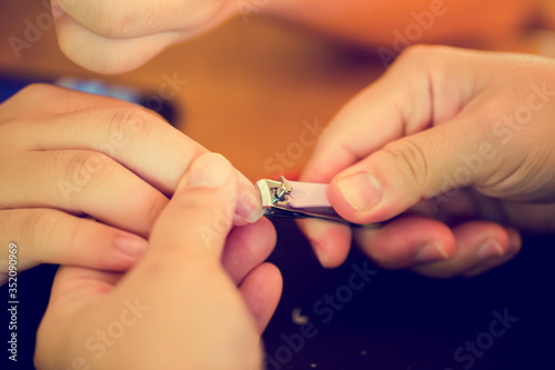 Selective focus to woman cutting nails to a hygiene child. Female hands hold nail scissors and child s hand. Manicure for kid by hand of scissor to cut nail for clean.