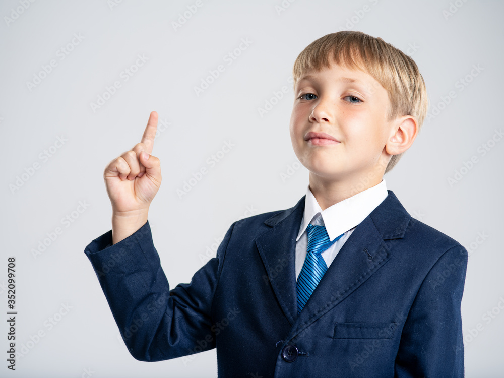 Photo of a businessman boy pointing finger up. Portrait of white kid in a blue business suit with an idea. 8 years old child dressed in a business formal suit with tie with an idea. Photo of a businessman boy pointing finger up. Portrait of white kid in a blue business suit with an idea. 8 years old child dressed in a business formal suit with tie with an idea.