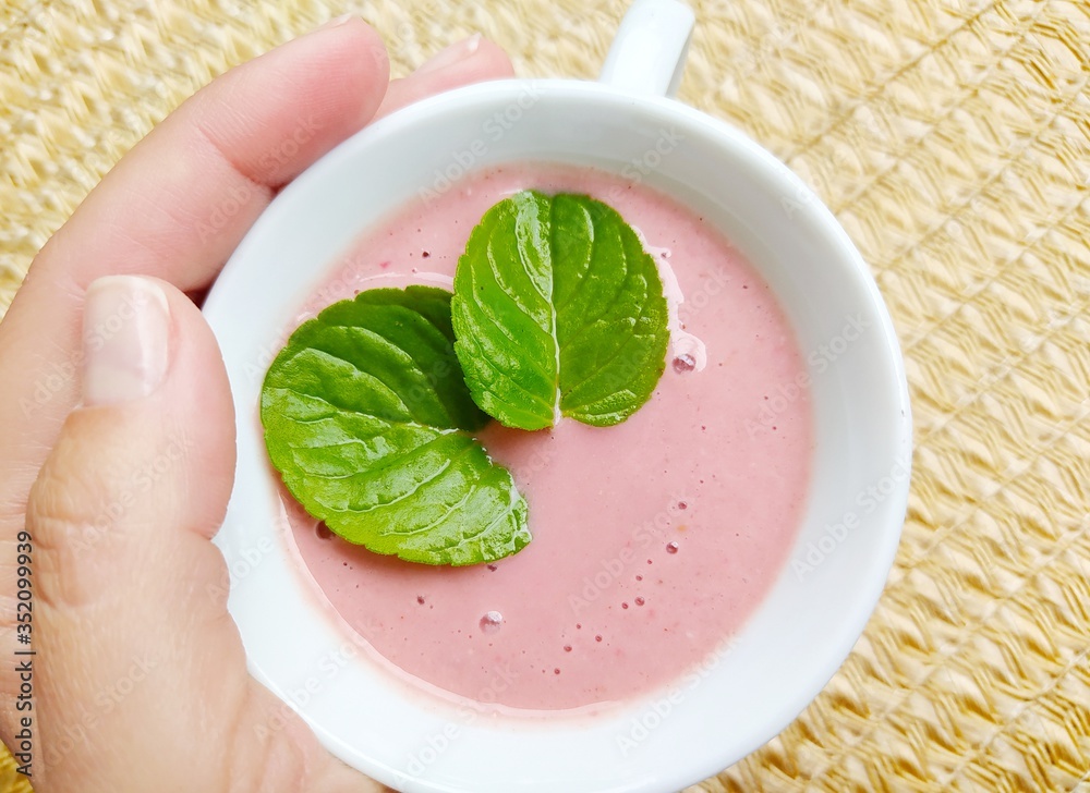 Woman's hand holding cup of strawberry smoothie with mint leaves Woman's hand holding cup of strawberry smoothie with mint leaves