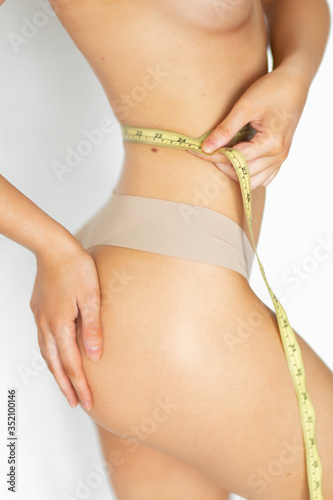A woman with an excellent figure measures the size of her waist with a centimeter. White background. Healthy lifestyle and a beautiful female figure. Losing weight.