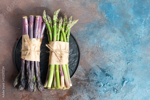 Fresh natural organic two bundles of green and purple asparagus vegetables on a dark stone background.