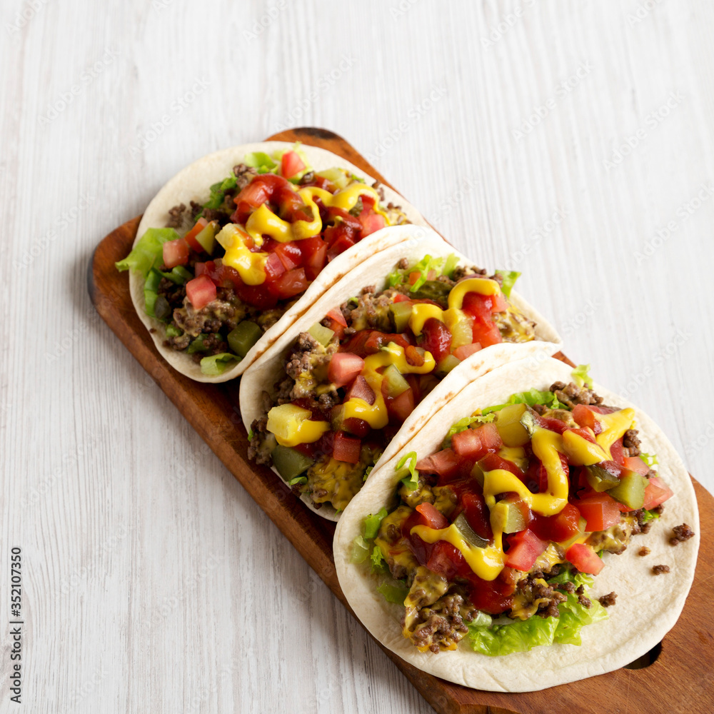 Homemade Cheeseburger Tacos on a rustic wooden board on a white wooden surface, low angle view. Homemade Cheeseburger Tacos on a rustic wooden board on a white wooden surface, low angle view.
