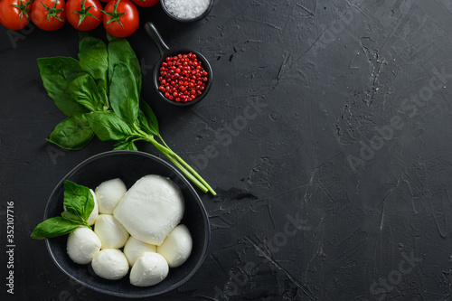 Mini balls of mozzarella cheese,Fresh cherry tomatoes, basil leaf, cheese for caprese salad on black slate stone chalkboard with copyspace.  Top view