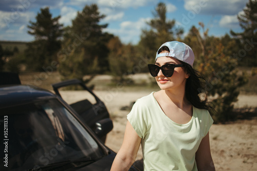 Young woman sitting on the car hood while traveling. Tourism lifestyle, vacation, freedom and travel concept