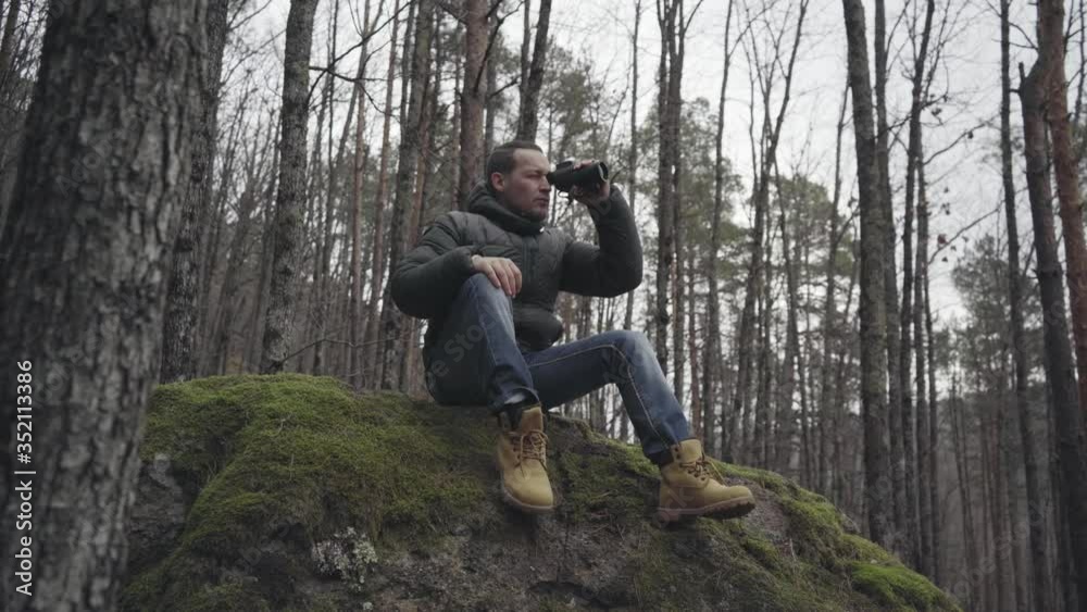 Traveler with monocle sitting on big stone in deep forest and looks into the distance. Traveler with monocle sitting on big stone in deep forest and looks into the distance.