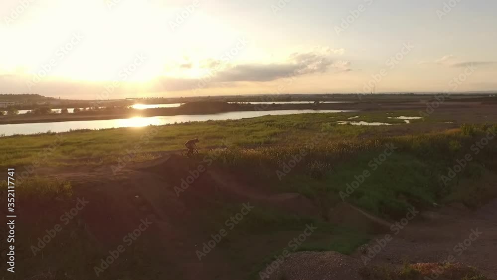Aerial shot of MTB biker doing stunt while riding on dirt ramp at sunset, drone flying over man cycling near river against sky - Erfurt, Germany Aerial shot of MTB biker doing stunt while riding on dirt ramp at sunset, drone flying over man cycling near river against sky - Erfurt, Germany
