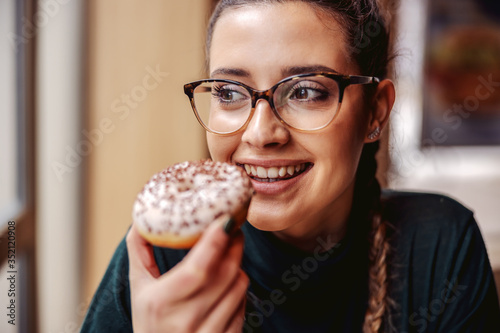 Portrait of smiling teenage girl sitting at pastry shop  holding doughnut and enjoying free time.