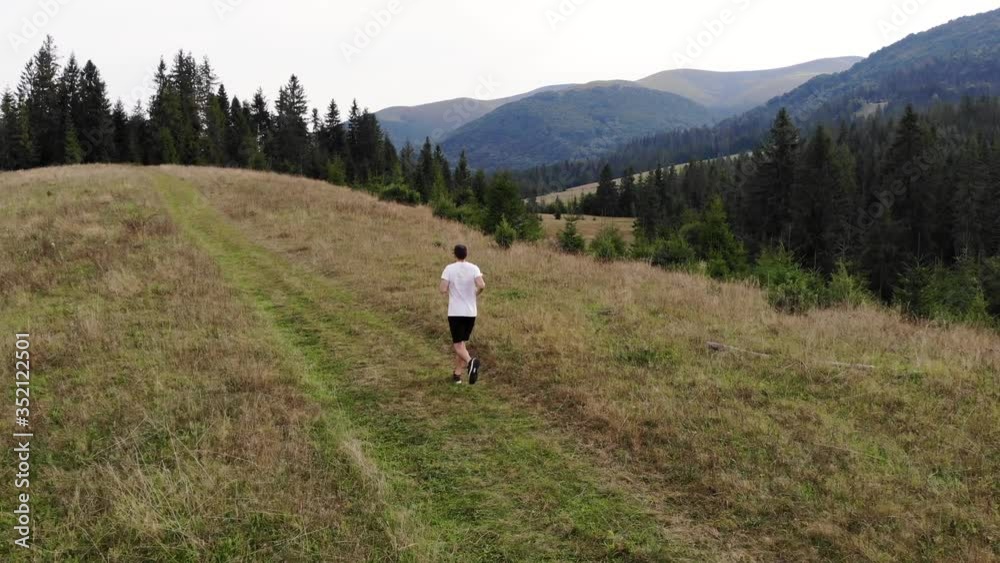Aerial drone view of man running in mountains forest with evergreen pine trees in countryside Aerial drone view of man running in mountains forest with evergreen pine trees in countryside