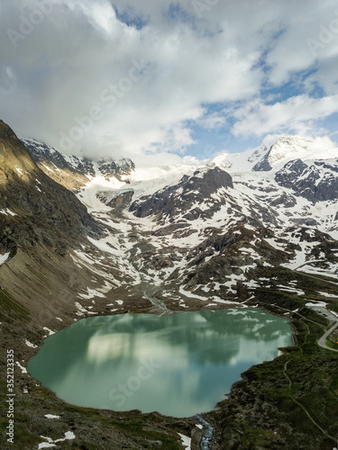 glacier lake in the swiss alps during spring with clouds, blue sky and snow taken with a drone