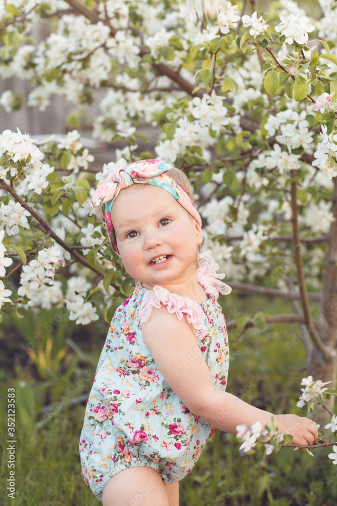 Cute baby girl on a background of white blossoms of an apple tree