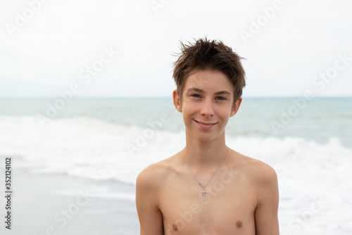 Handsome young boy at beach, summer vacation. Portrait of beautiful calm smiling teen boy at sea coast posing after swimming. Travel, summer vacation, tourism, teenage lifestyle, recreation © Khorzhevska