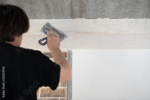 Putty knife in male hand. Hand workю Worker putsty plasterboard ceiling in new appartment. Repairman works with plasterboard, plastering dry-stone wall, home improvement. Man makes repairs at house.