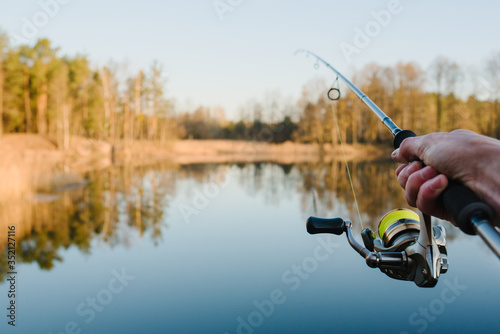 Fisherman with fishing rod in his hand catches fish on a boat. Fishing Day. Spinning in hand on pond background.