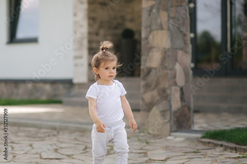 Adorable little girl walk near the house. Beautiful kid spend time in front of the house © Aleksandr