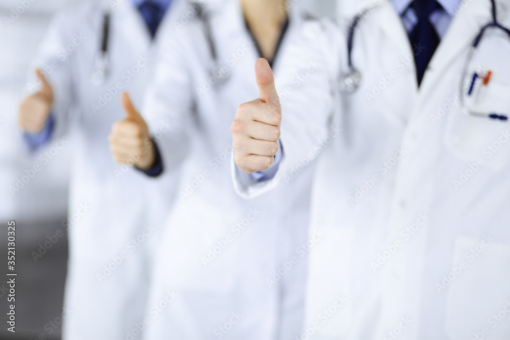 Group of unknown doctors stand as a team with thumbs up in a hospital office. Physicians ready to examine and help patients. Medical help, insurance in health care, best desease treatment and medicine Group of unknown doctors stand as a team with thumbs up in a hospital office. Physicians ready to examine and help patients. Medical help, insurance in health care, best desease treatment and medicine