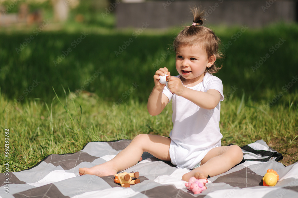 Happy little kid sits outdoors on carpet and play with toy animals. Adorable little girl in white bodysuit Happy little kid sits outdoors on carpet and play with toy animals. Adorable little girl in white bodysuit