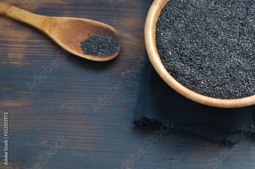 black sesame close up shot in wooden spoon and wooden bowl on a wooden background