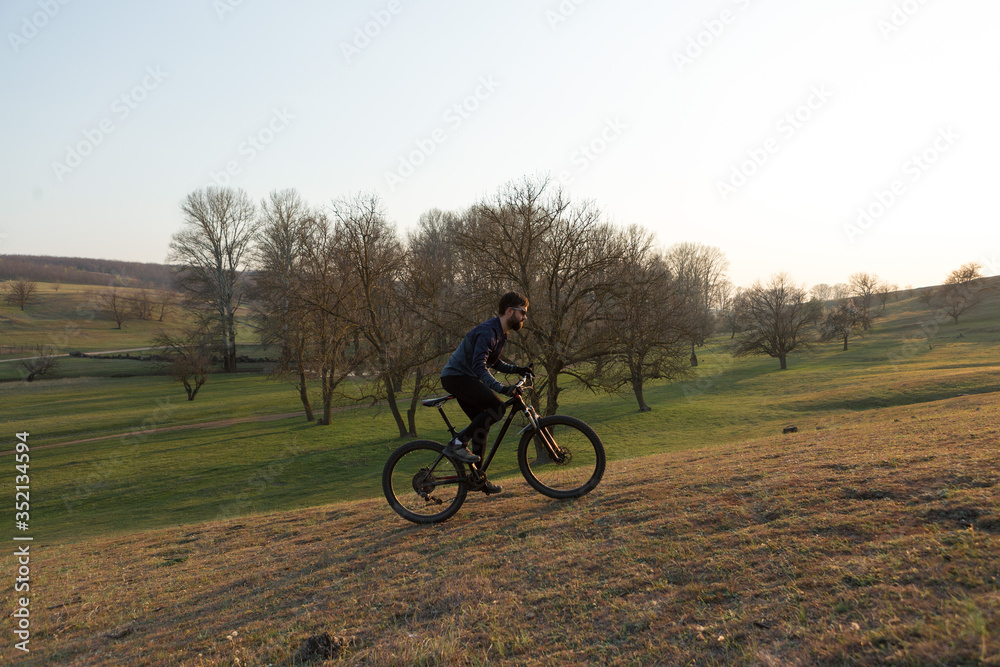 Fototapeta premium Cyclist in shorts and jersey on a modern carbon hardtail bike with an air suspension fork standing on a cliff against the background of fresh green spring forest