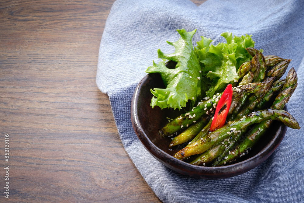 Stir fried asparagus with garlic and Teriyaki sauce in bowl on wooden table background with denim tablecloth. Asian wok vegetables. Healthy vegetarian food. Restaurant menu. Close up, copy space