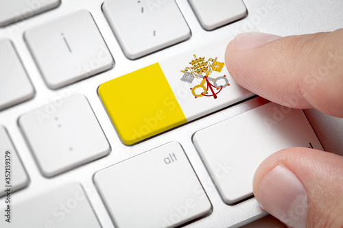 Online International Business concept: Computer key with the Vatican on it. Male hand pressing computer key with Vatican flag.