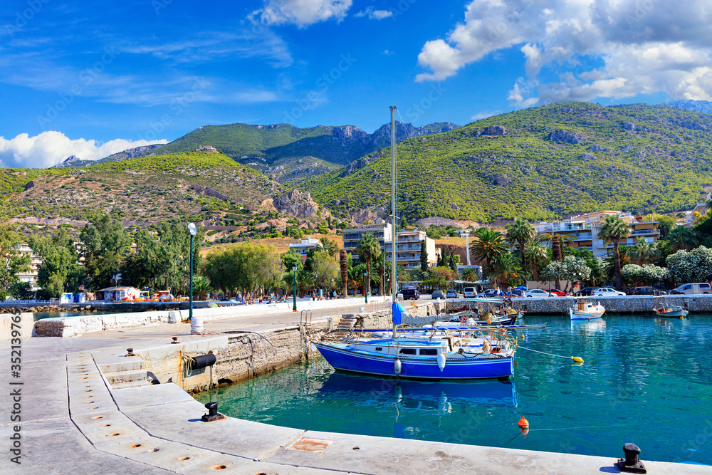 Obraz premium Scenic view of the bay and pier Loutraki, Greece, where small fishing schooners, yachts, boats and boats moored in the clear waters of the Ionian Sea.
