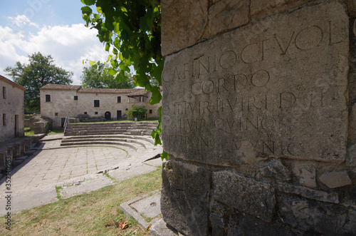 In the foreground an epigraph written in Latin and in the background a part of the amphitheater. Archaeological site of Altilia. Sepino - Molise - Italy photo