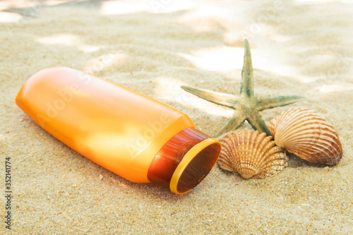 bottle of suntan lotion or sun cream on the beach sand with sea shell
