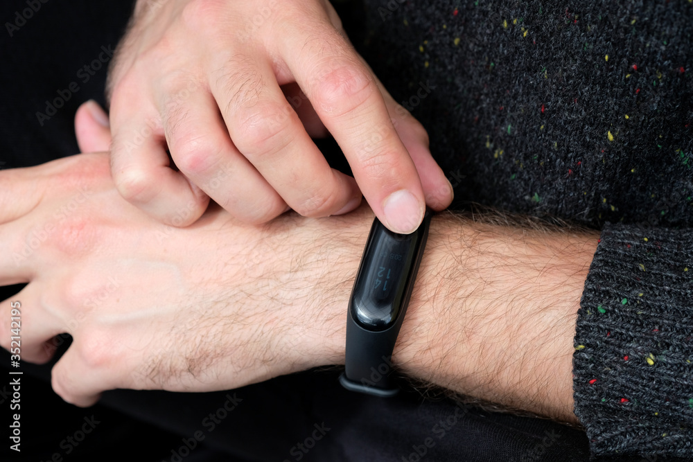black fitness bracelet on the guy’s hand closeup. Concept of modern gadgets for sports and healthcare. Young guy touching smart band after running in the morning. Pedometer Fitness device.