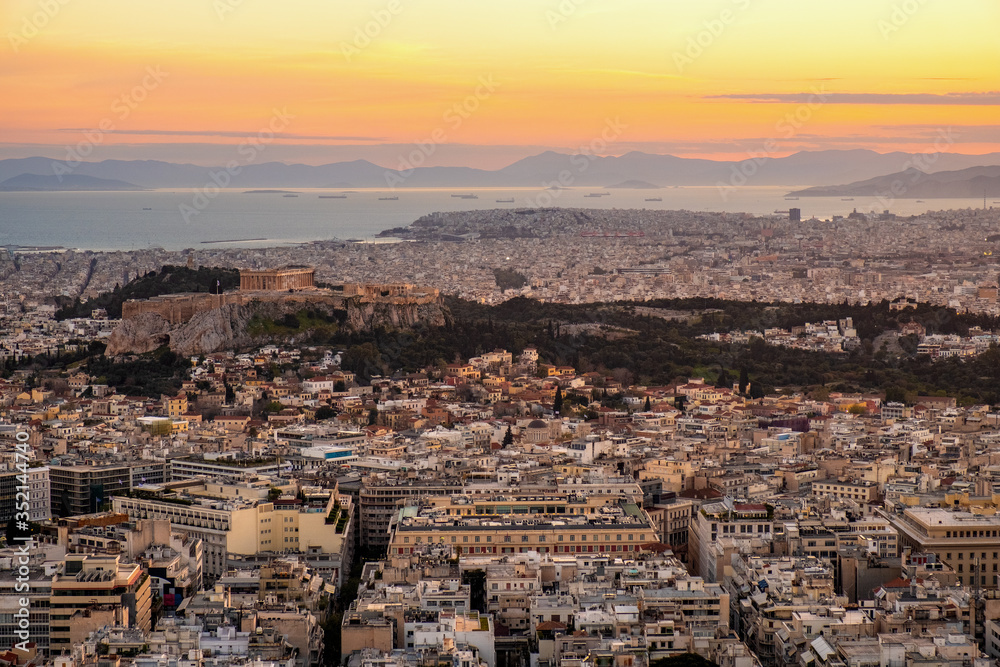 Panoramic sunset view of Athens, Greece, with Acropolis hill and Piraeus port at Saronic Gulf of Aegean sea in background seen from Lycabettus hill