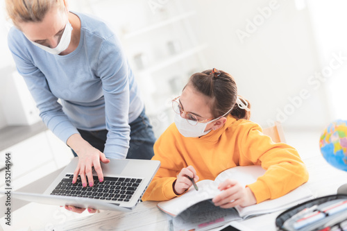 Child home studying education, homeschooling, with private tutor / mother with protective mask in the time of viruses, flu and seasonal pandemic, healthy approach in social contact.