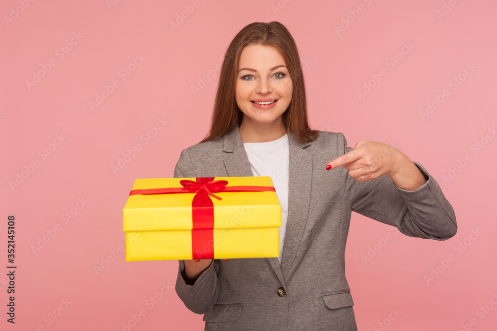 Portrait of joyful elegant businesswoman in suit jacket pointing at present, celebrating anniversary, showing bonus gift for her success at work, promotion. studio shot isolated on pink background Portrait of joyful elegant businesswoman in suit jacket pointing at present, celebrating anniversary, showing bonus gift for her success at work, promotion. studio shot isolated on pink background