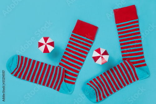 Fototapeta Naklejka Na Ścianę i Meble -  two socks with red stripes, as if walking, on a turquoise background, next to two umbrellas, the concept of travel