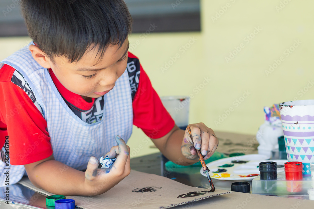 Portrait image of 5-6 yeas old child boy. Asian student drawing and painting colours on the paper in the room. Study​ from​ home, social​ Distance, Kid and education concept.