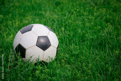 Soccer ball on the lawn on sunny summer day, close-up. White and black ball on background of green grass, copy space. Concept of active recreation, sports entertainment in nature.