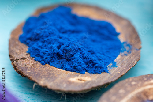 Blue food coloring powder in a coconut plate on a cyan table top. Close up of a blue powder.